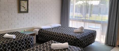 Habitación de hotel con dos camas, una ventana con cortinas, una pared con diseño de ladrillos y un reloj.