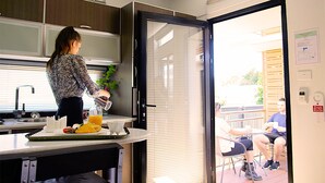 A modern kitchen with a large window, a dining area with outdoor seating, and a door leading to an outdoor patio. - Room Motel Kingaroy (Kingaroy)