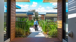 A man walking on a pathway between buildings with a clear sky above. - Room Motel Kingaroy (Kingaroy)