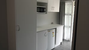 A compact kitchenette with white cabinets, a microwave, and a refrigerator.