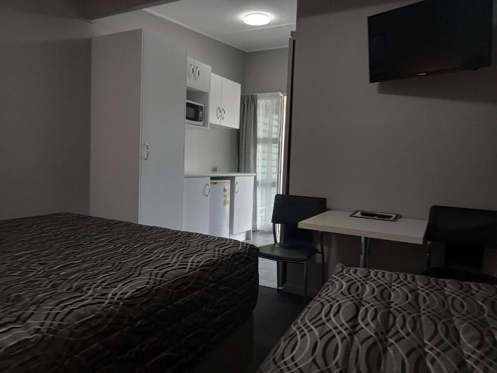 Habitación de hotel con dos camas, un escritorio, una silla, un televisor y una kitchenette.