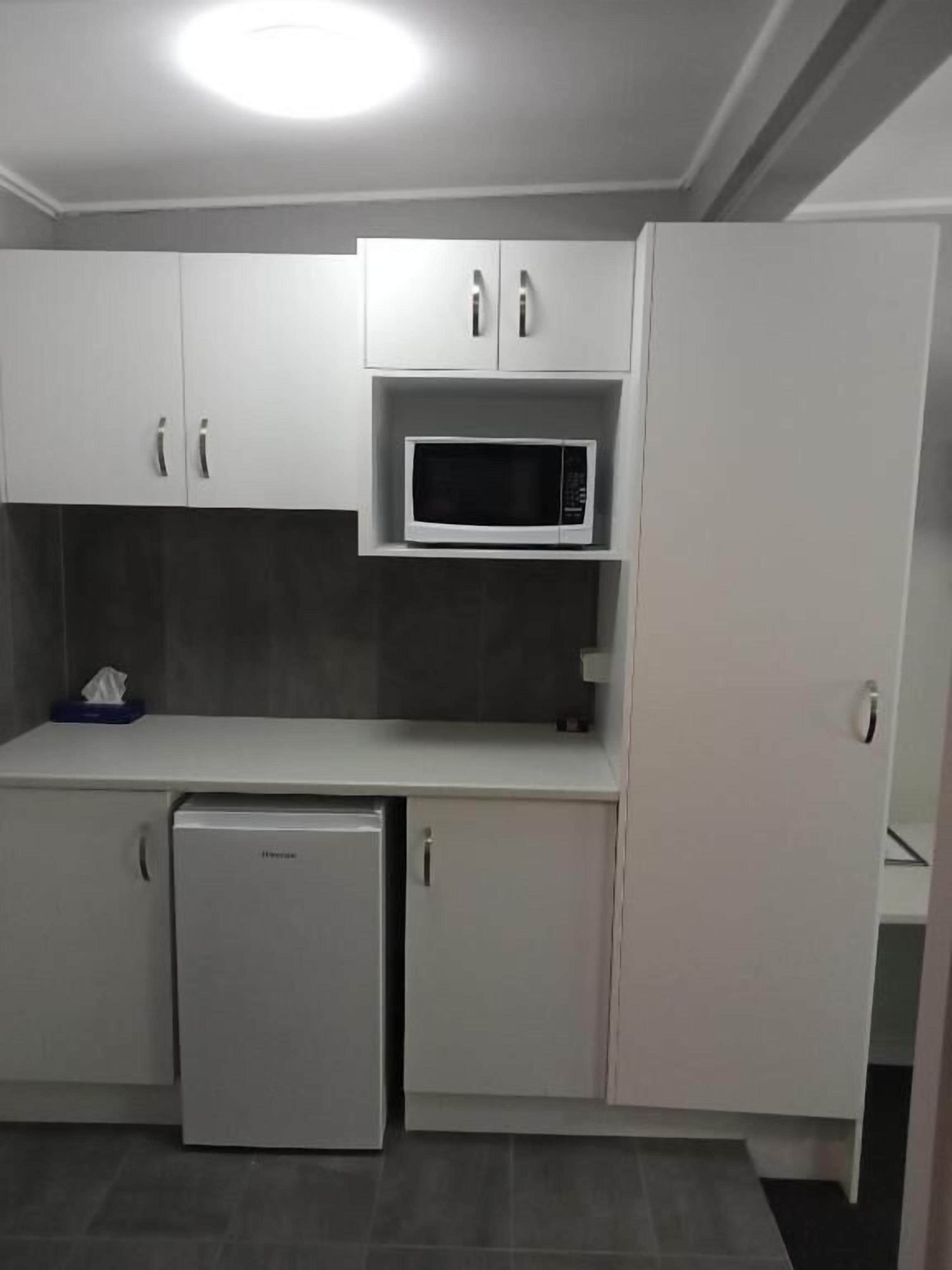 A compact kitchen with white cabinets, a microwave, and a mini-fridge.