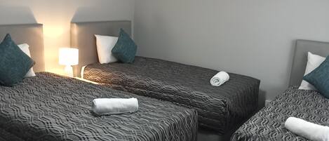 Habitación de hotel con dos camas, cada una con cabecera, lámpara de noche y una toalla enrollada sobre la cama.