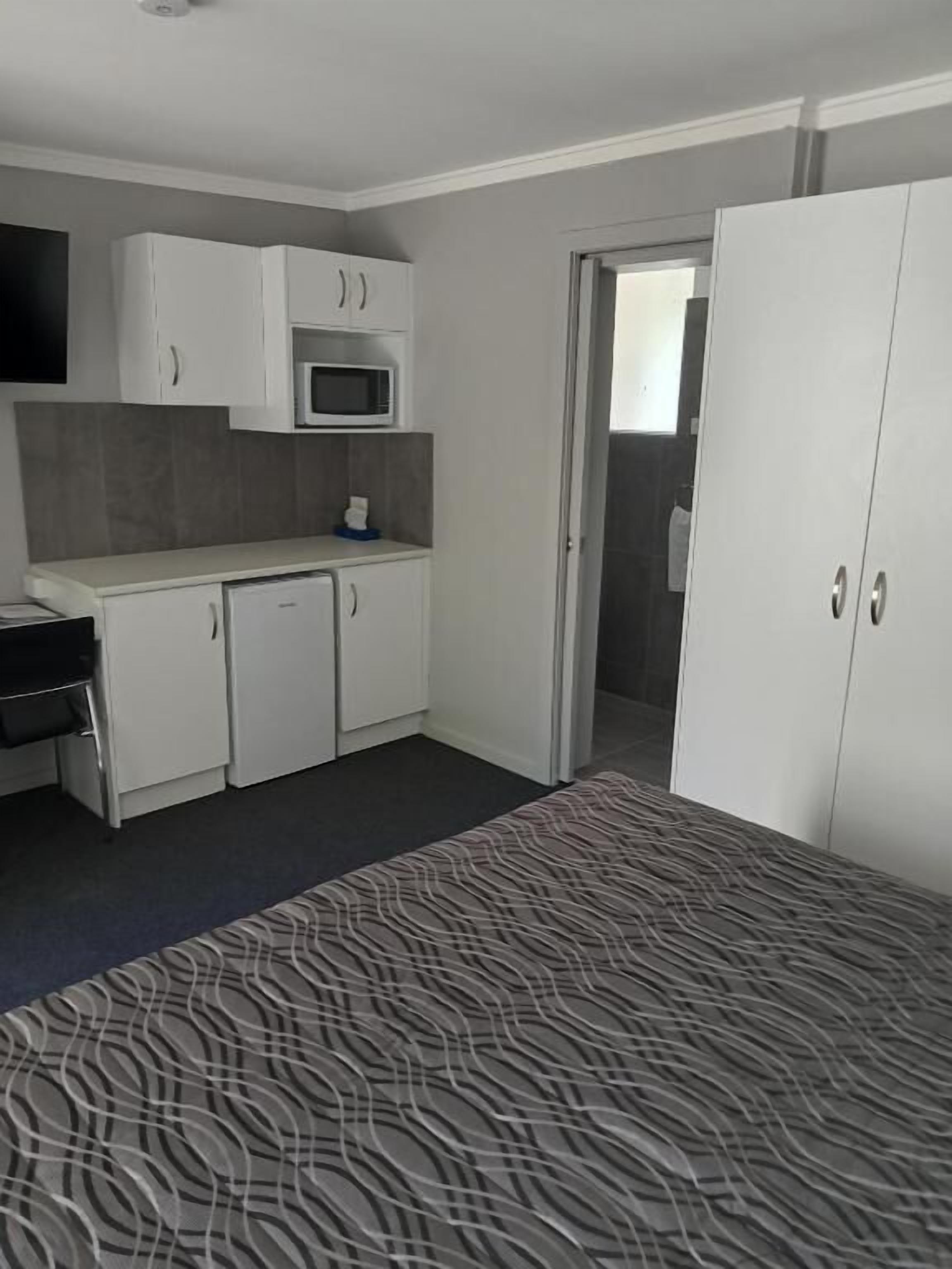 Une pièce compacte comprenant un coin cuisine, un lit avec une couvre-lit à motifs et une armoire.