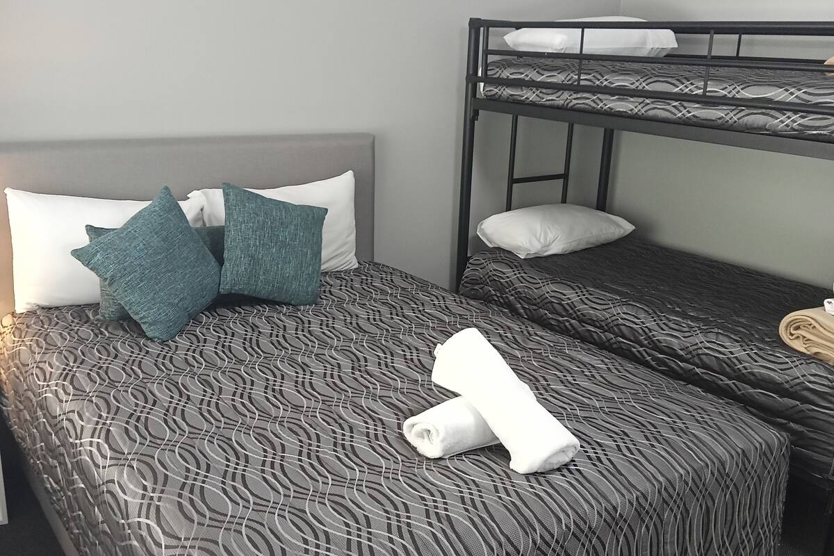 Quarto de hotel com uma cama grande, uma cama beliche e uma mesinha.