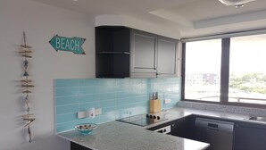 Una cocina con salpicadero azul, un lavamanos, un lavavajillas y una ventana con vistas a edificios.