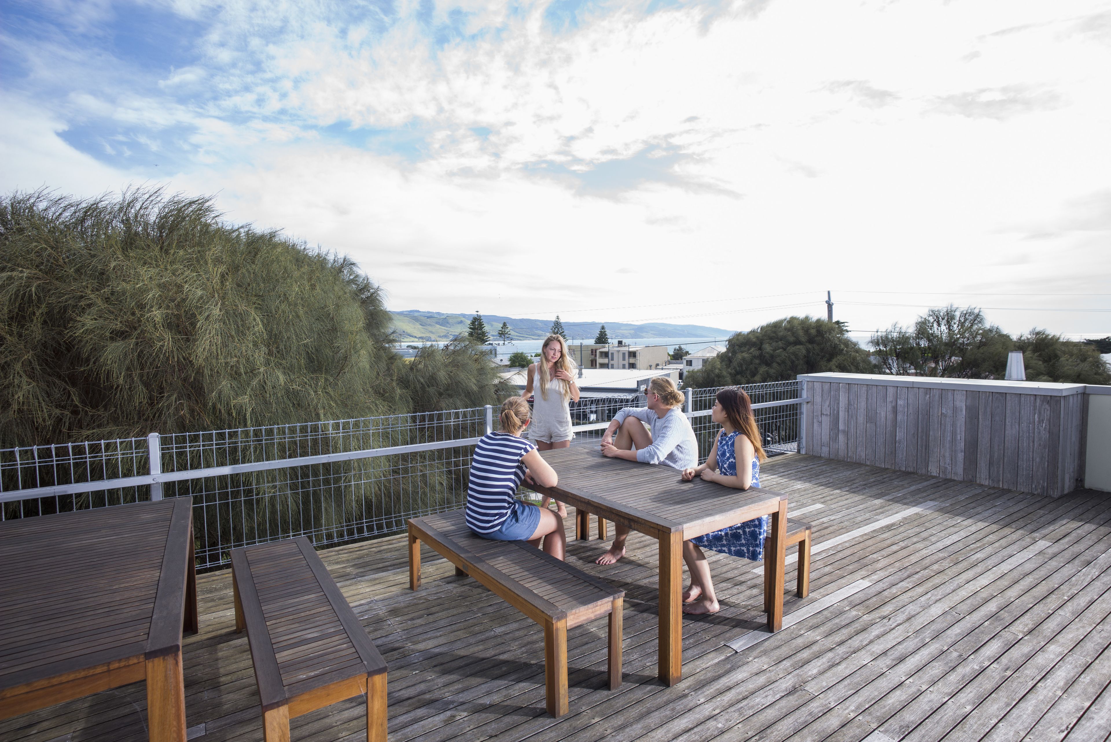 Een houten terras met banken en tafels, met uitzicht op een waterpartij en heuvels.