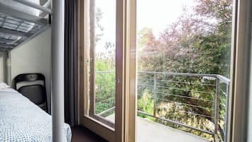 A hotel room with a bed, a chair, and a balcony with a view of trees.