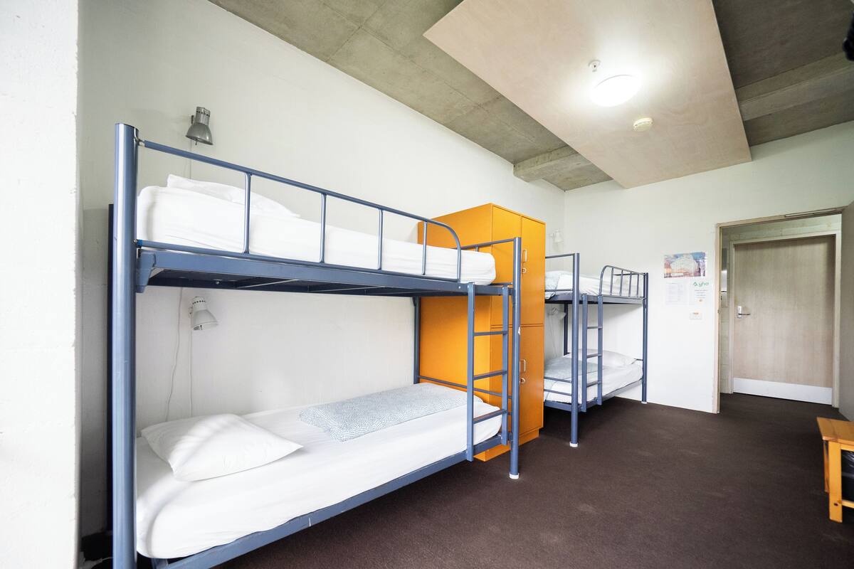 A dormitory room with bunk beds, a wooden door, and a small table.