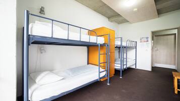 A dormitory room with bunk beds, a wooden door, and a small table.