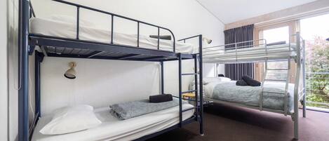 A dormitory room with bunk beds, a desk, and a window with curtains.