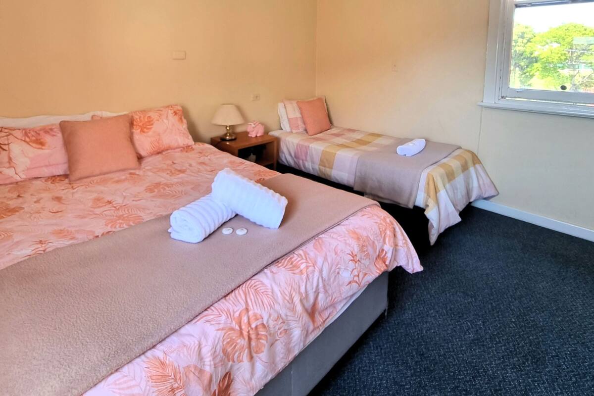 Habitación de hotel con dos camas, cada una con ropa de cama y almohadas estampadas con motivos florales. Se ve vegetación a través de la ventana.