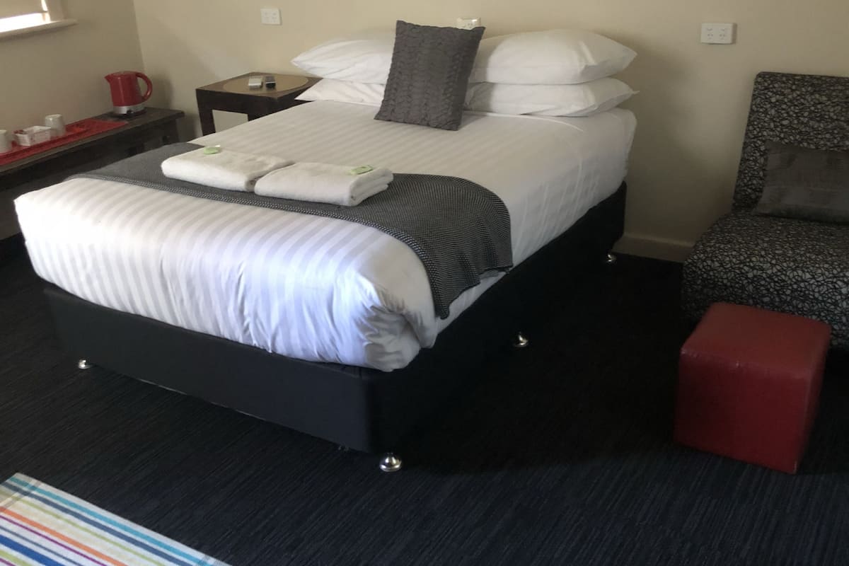 Una habitación de hotel con una cama, mesita de noche, silla y un pequeño otoman rojo.