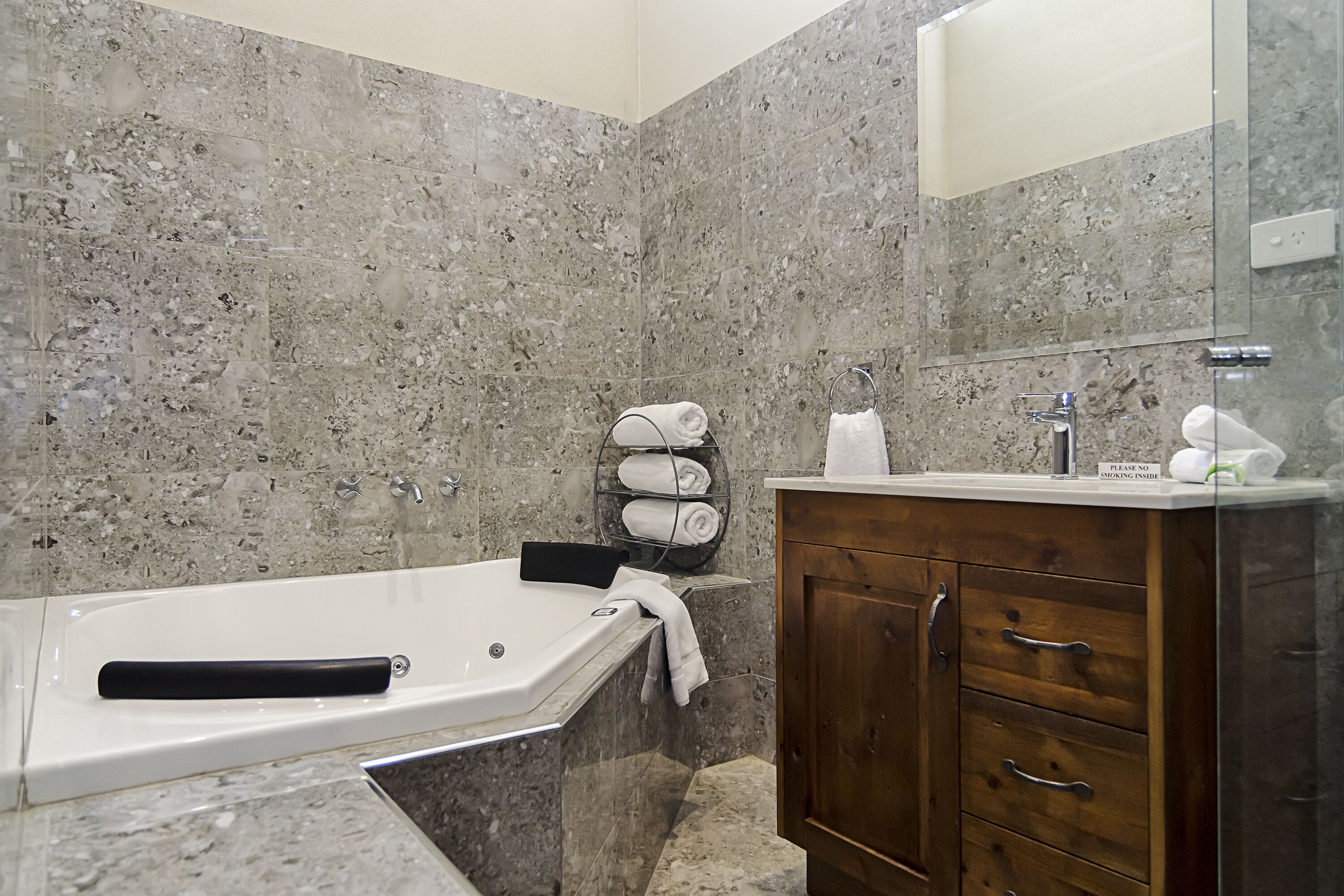 A modern bathroom with a marble wall, a wooden vanity, and a bathtub.