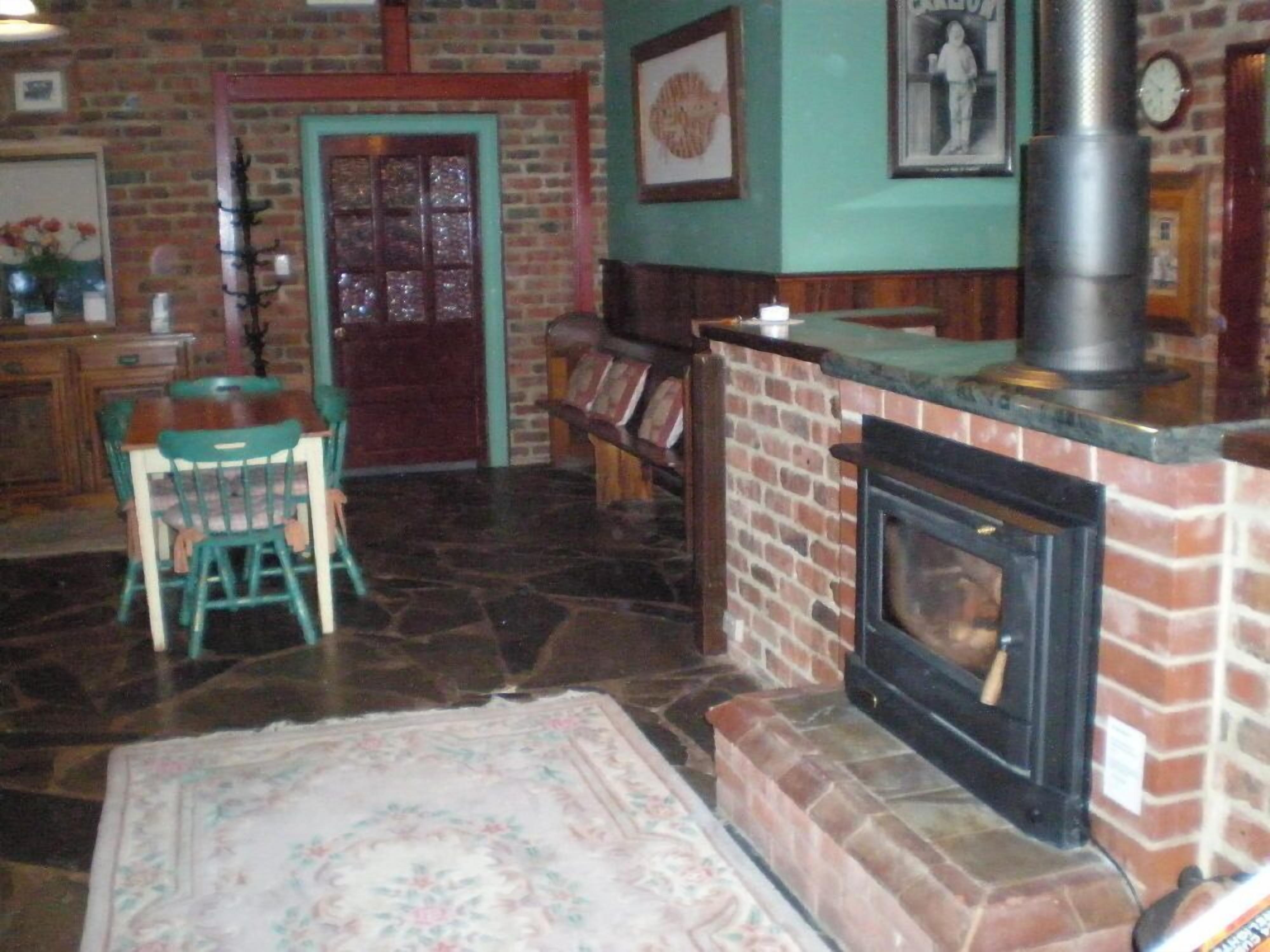 Una habitación acogedora con chimenea de ladrillo, una mesa de madera con sillas y un tapete estampado en el suelo.