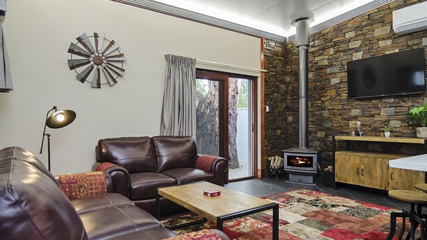 A cozy living room with a leather sofa, a coffee table, a fireplace, and a stone wall. - Eagle Foundry Bed & Breakfast (Gawler)