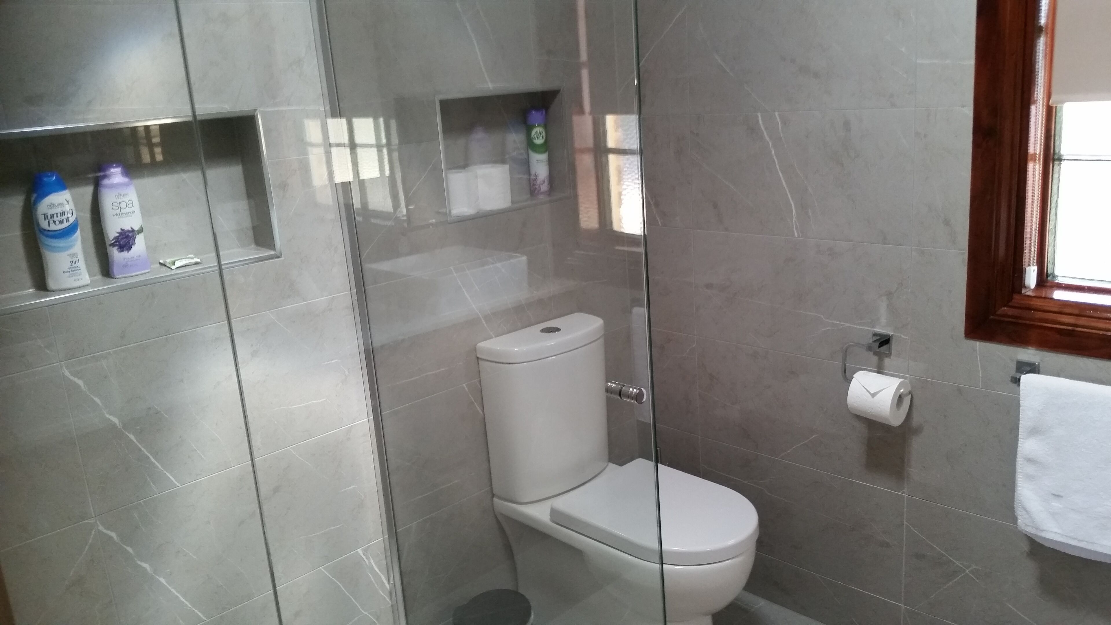 Uma casa de banho moderna com sanita, cabine de duche em vidro e um armário com artigos de higiene pessoal.