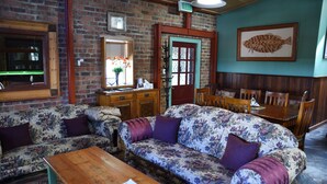 A cozy room with a brick wall, a wooden table, two floral sofas, a wooden bench, and a dining area with chairs and a table. - Eagle Foundry Bed & Breakfast (Gawler)
