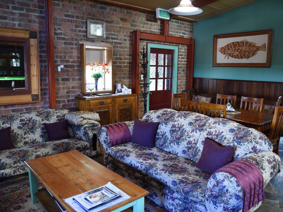 A cozy room with a brick wall, a wooden table, two floral sofas, a wooden bench, and a dining area with chairs and a table.