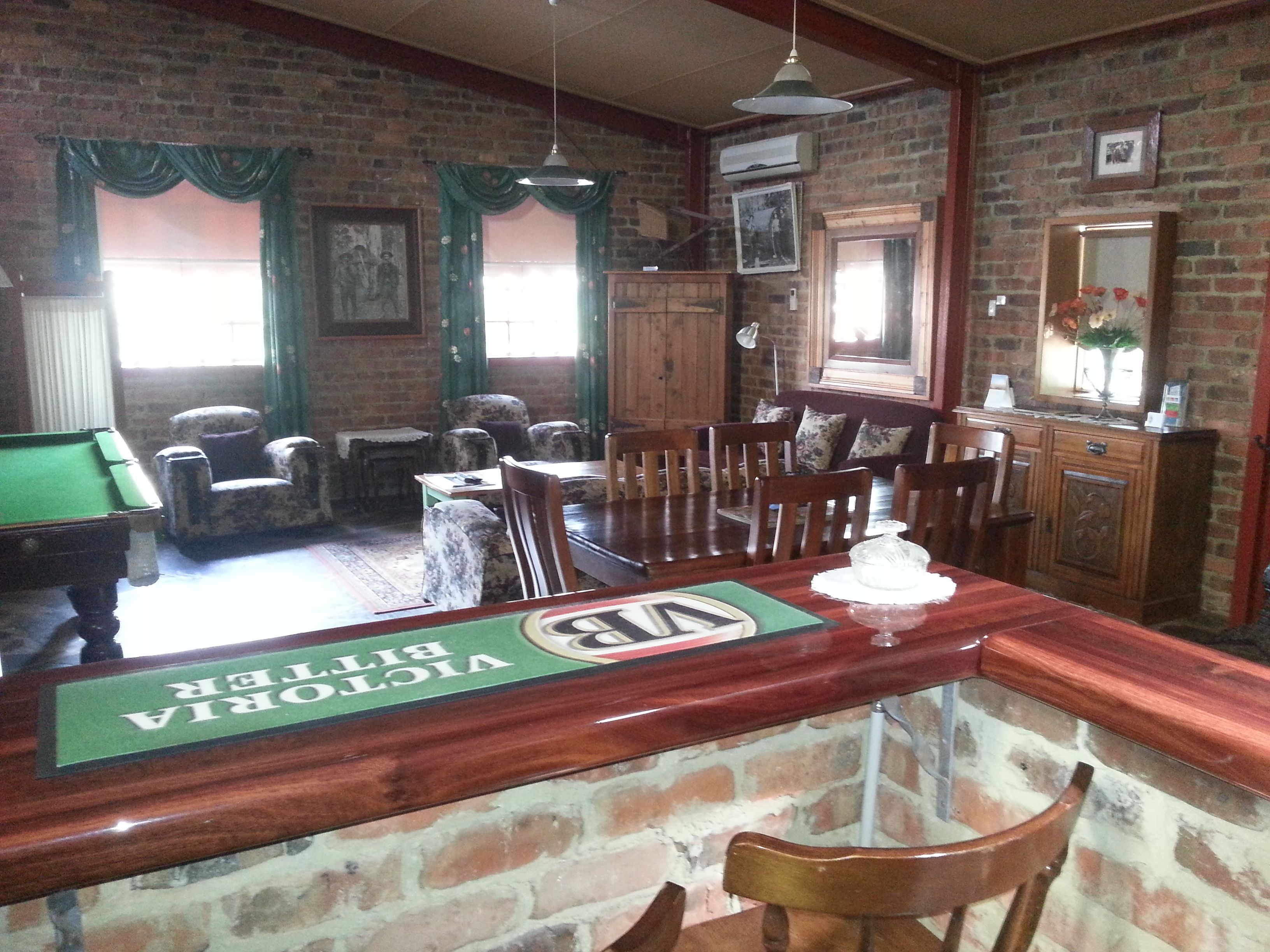 A billiards room with a pool table, chairs, and a bar area with a sign.