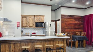 A kitchen with wooden cabinets, a microwave, a refrigerator, and a bar area with stools. - Eagle Foundry Bed & Breakfast (Gawler)