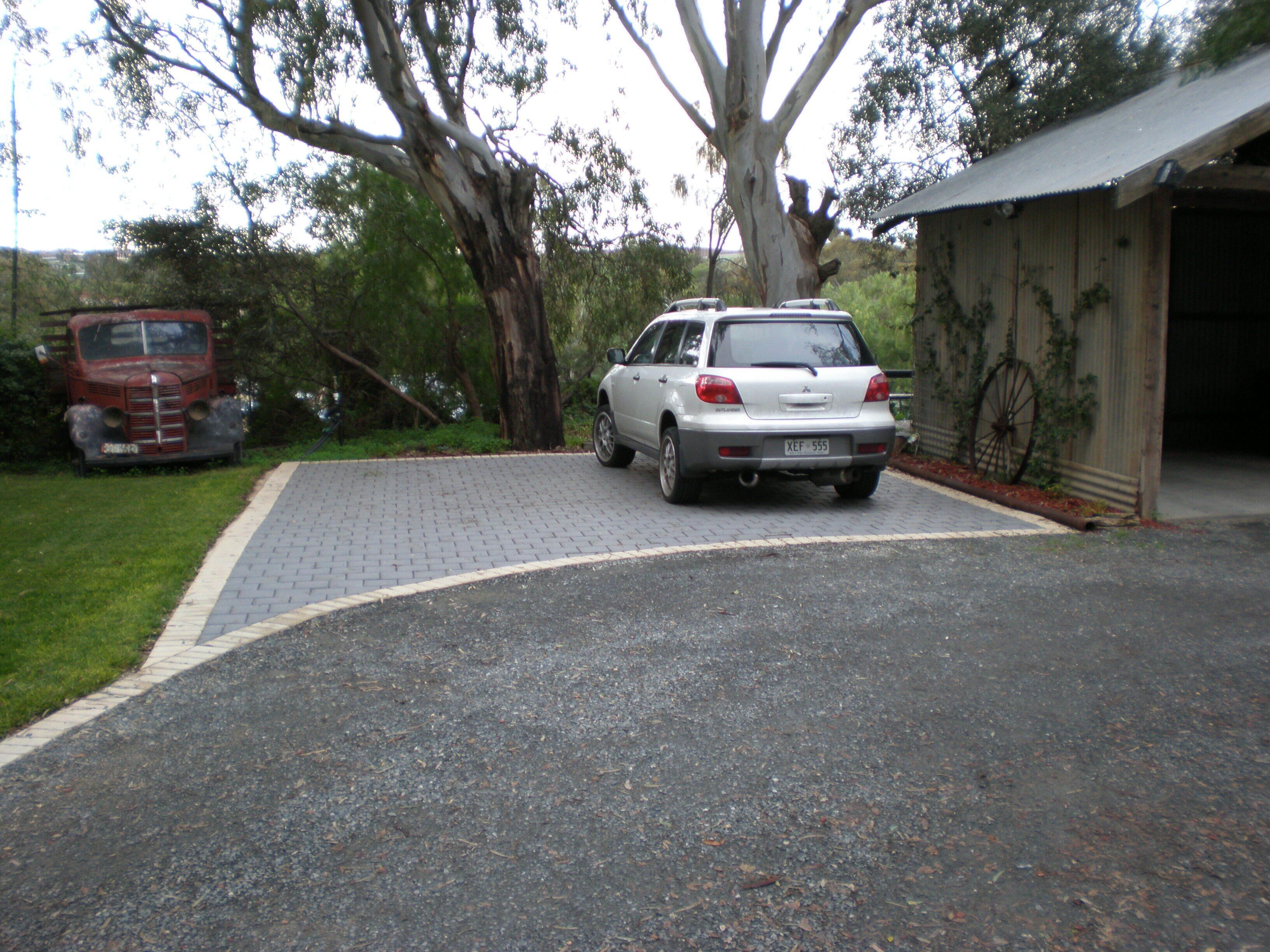 A silver car parked in a driveway with a red truck in the background.