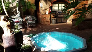 A small outdoor swimming pool with a brick patio, wicker furniture, and a brick wall with a window. - Eagle Foundry Bed & Breakfast (Gawler)