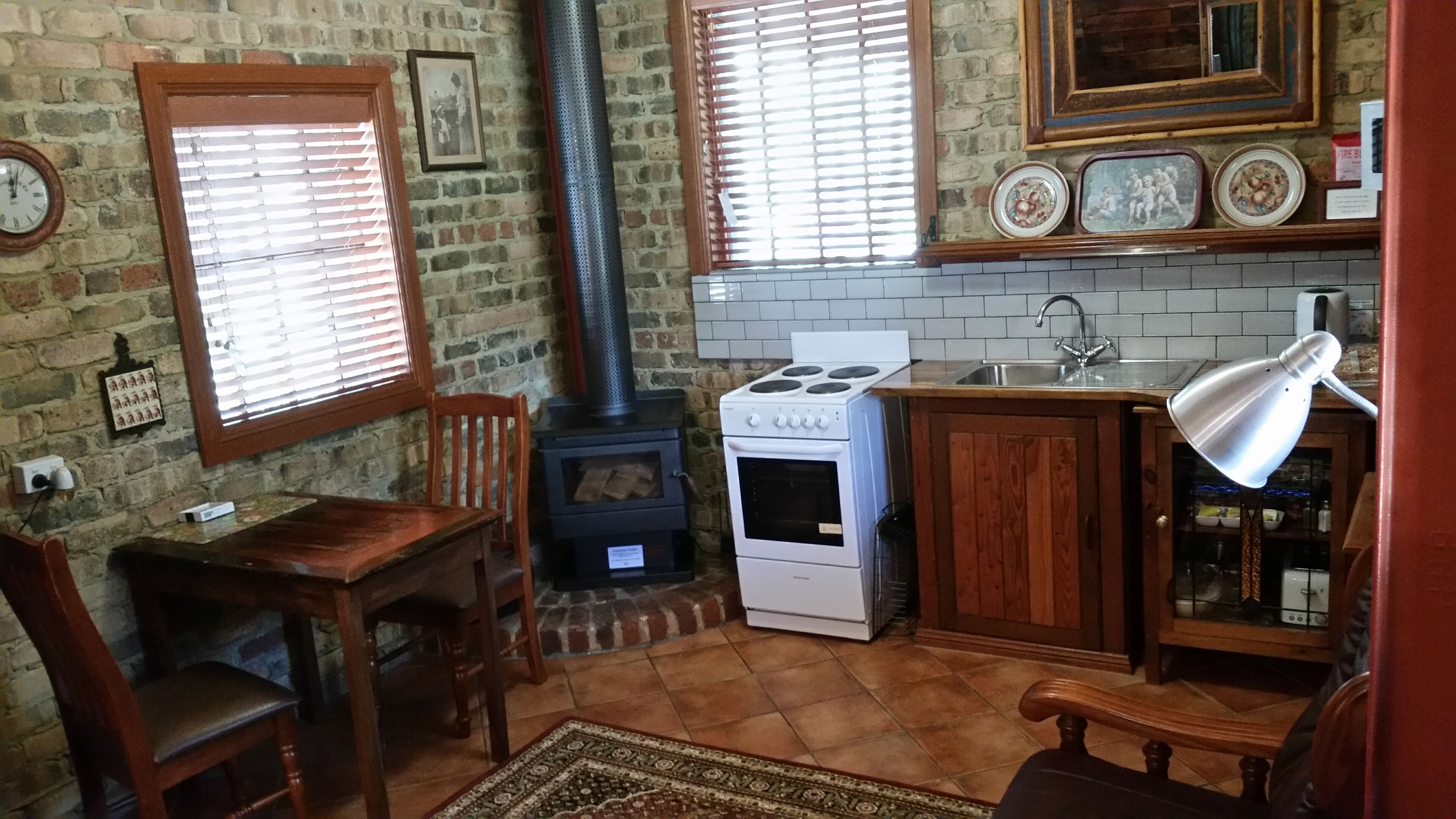 Una cocina con estufa de leña, estufa blanca y un lavamanos con grifo. Hay una silla y una mesa con alfombra.