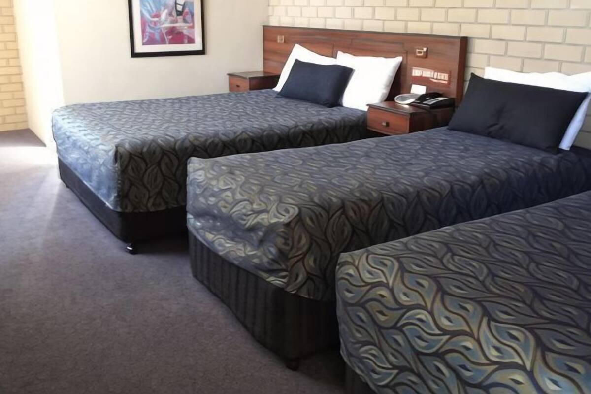 Quarto de hotel com duas camas, uma mesa de cabeceira, um telefone e uma parede de tijolos.