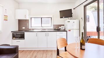 A modern kitchen with white cabinets, a microwave, a coffee maker, and a table with a bottle of wine and two glasses.