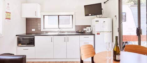 Eine moderne Küche mit weißen Schränken, einer Mikrowelle, einer Kaffeemaschine und einem Tisch mit einer Weinflasche und zwei Gläsern.