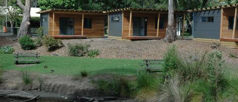 A row of wooden cabins with large windows and a small pond in the foreground.