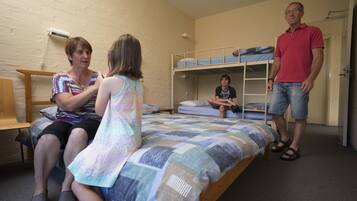 A dormitory room with bunk beds, a desk, and a chair.