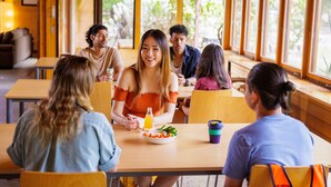 Un grupo de personas sentadas alrededor de una mesa en un espacio interior luminoso con grandes ventanales.