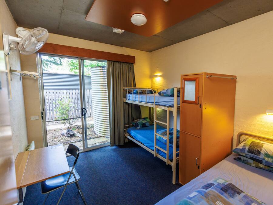 A dormitory room with bunk beds, a desk, a chair, and a fan.