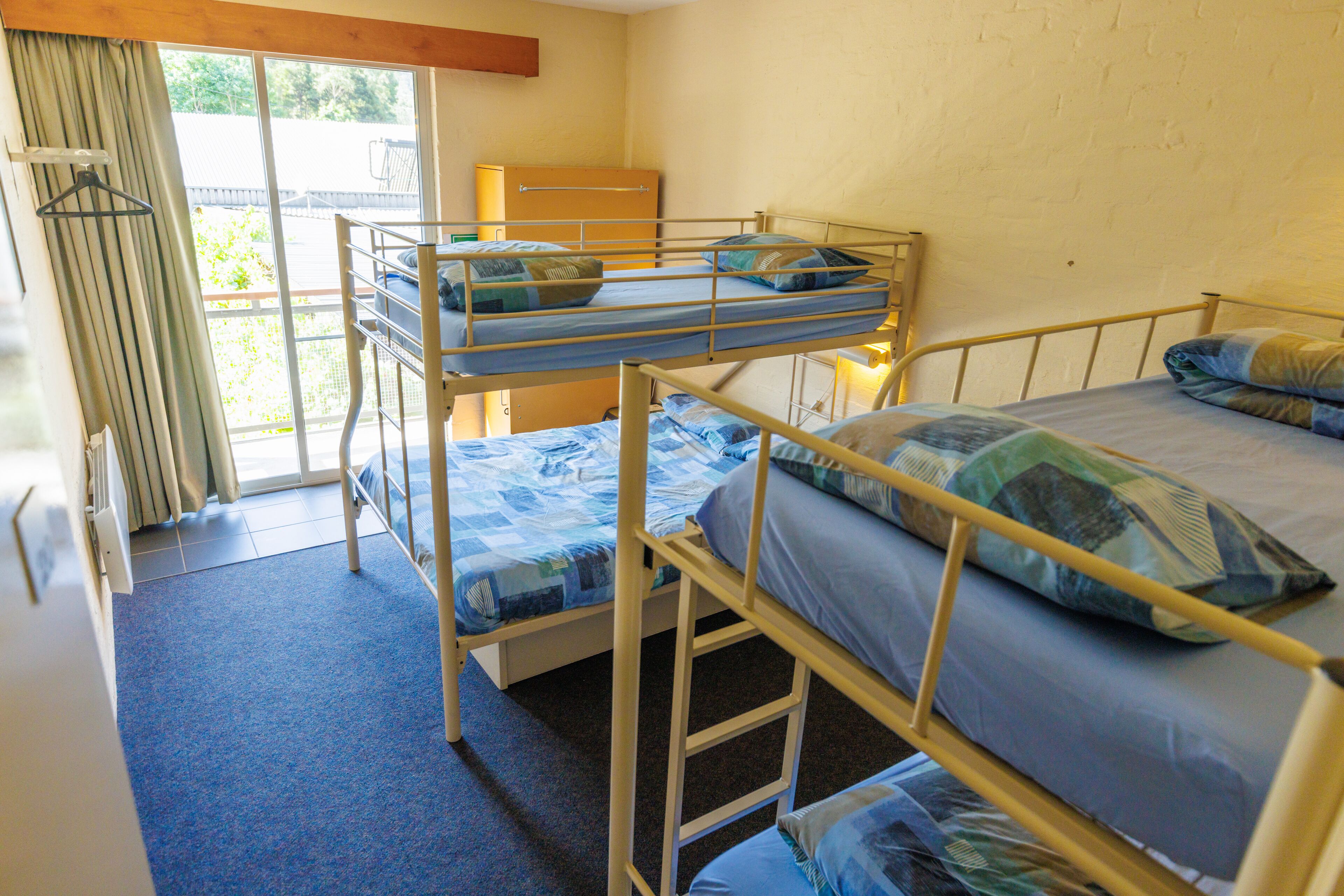 Une chambre de dortoir avec des lits superposés, une fenêtre avec des rideaux et une porte donnant sur l’extérieur.