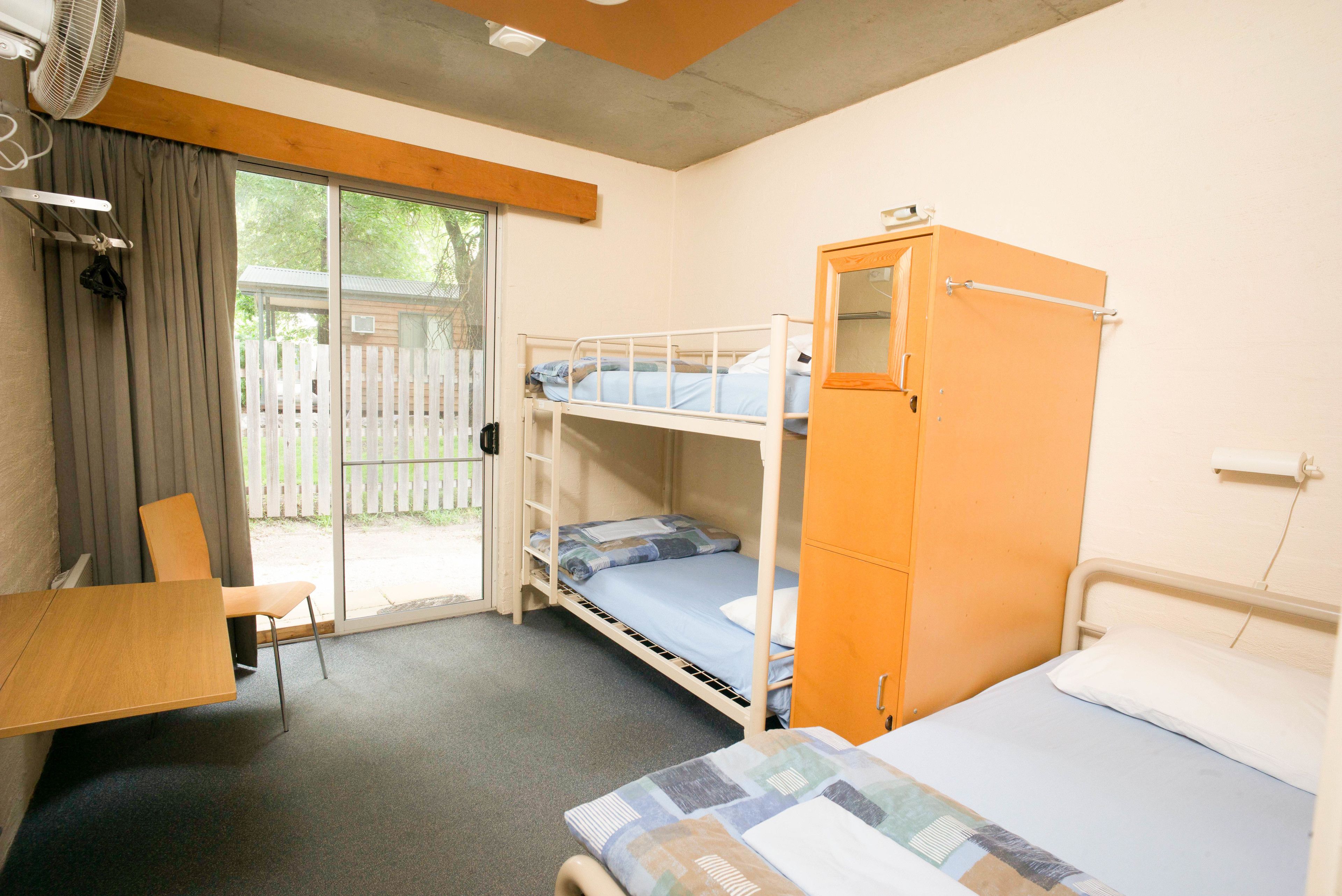 Una habitación tipo dormitorio con literas, un escritorio, una silla y un armario.