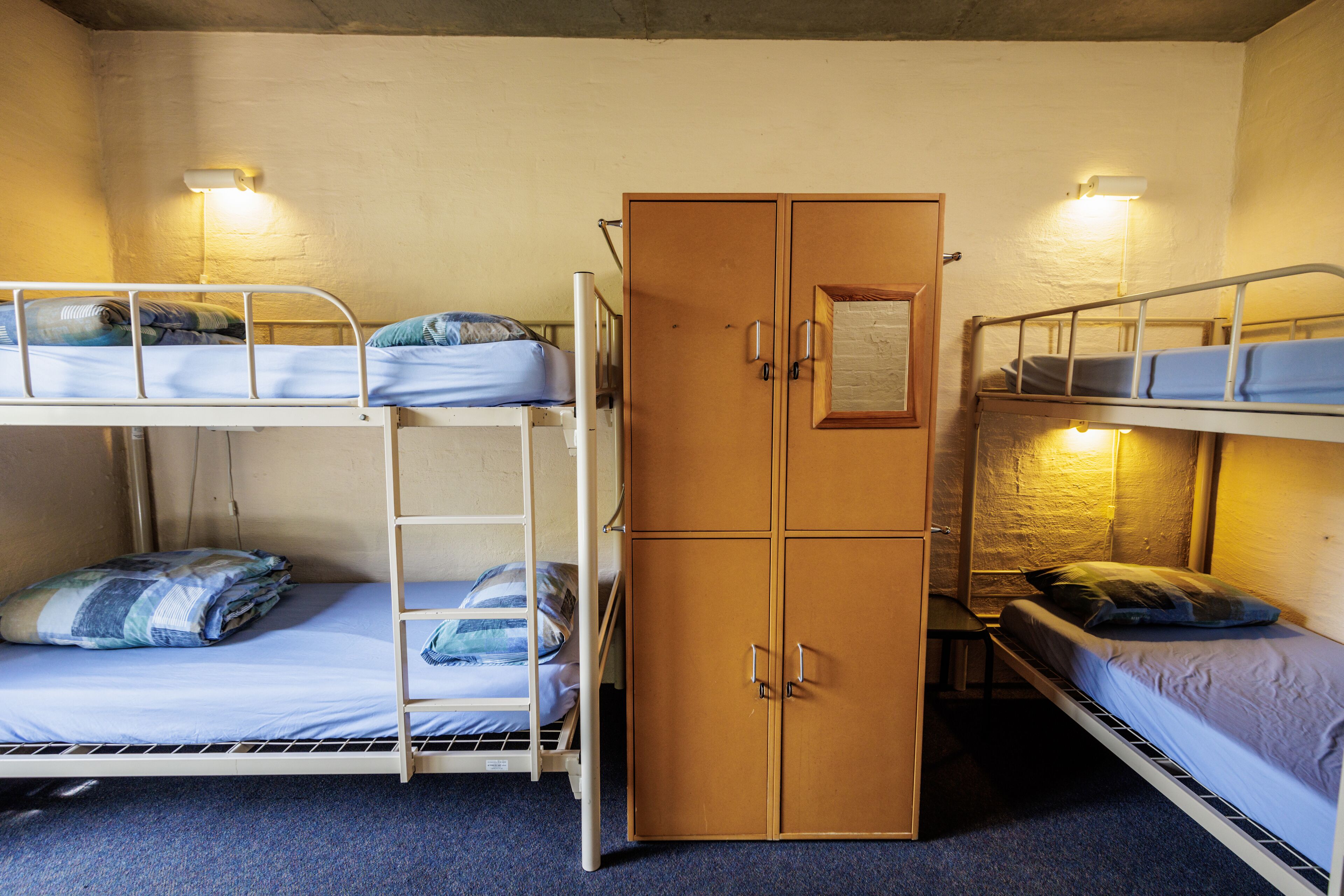 A dormitory room with bunk beds, a wardrobe, and two bedside lamps.