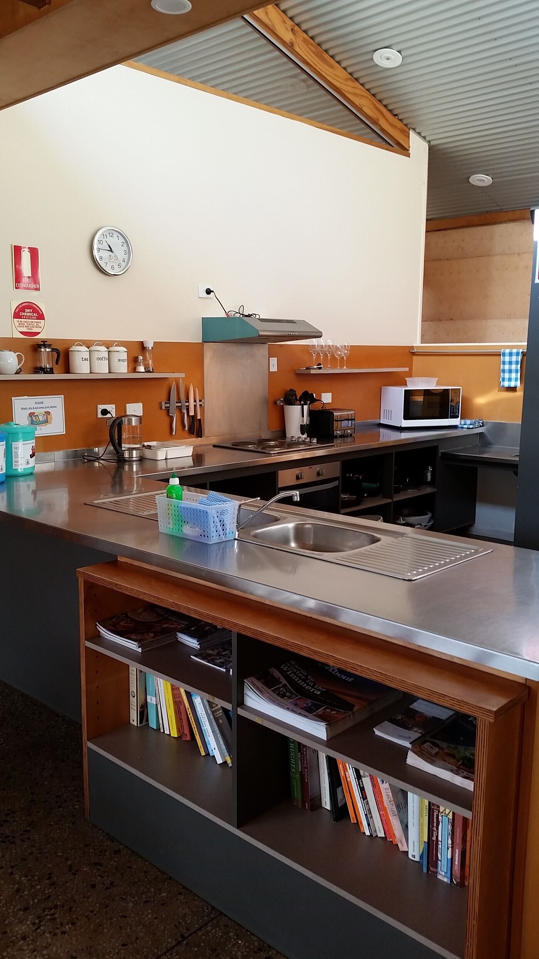 A modern kitchen with stainless steel appliances, a sink, and a built-in bookshelf with books.