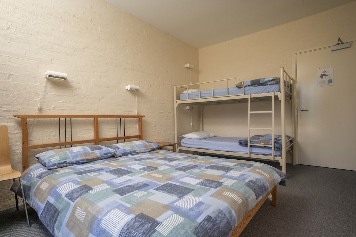 Habitación tipo dormitorio con una cama individual, una litera, una silla de madera y un escritorio.