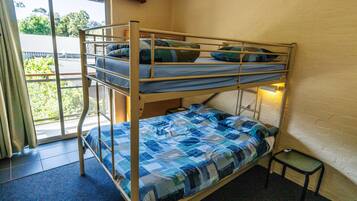 A bunk bed with blue bedding, a small table, and a window with a view of greenery.