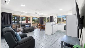 A modern living area with a sofa, a dining table, and a kitchen with a refrigerator and a TV. - Alexander Beachfront Apartments (Torquay)