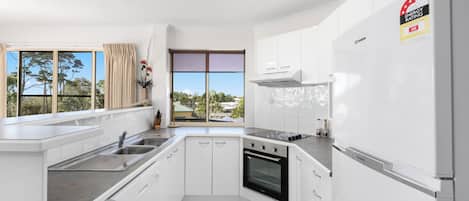 Una cocina moderna con armarios blancos, horno empotrado, pileta de acero inoxidable y refrigerador.