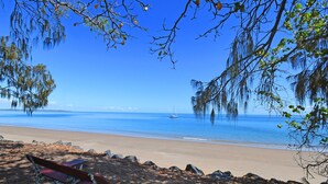 A beach with a bench, clear blue water, and a sailboat in the distance. - Alexander Beachfront Apartments (Torquay)