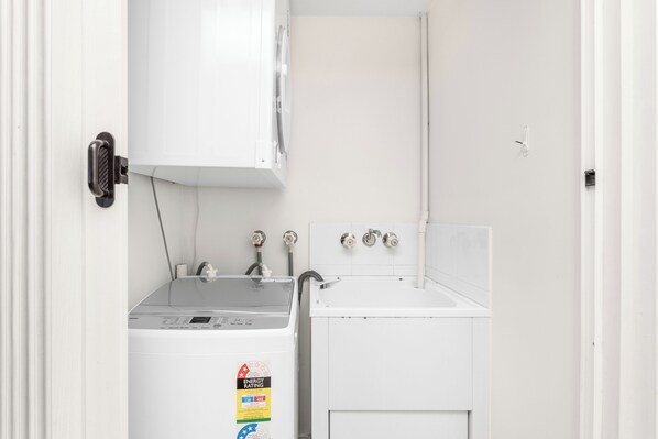 Un cuarto de lavandería con lavadora y secadora, ambos blancos, y un lavamanos pequeño.