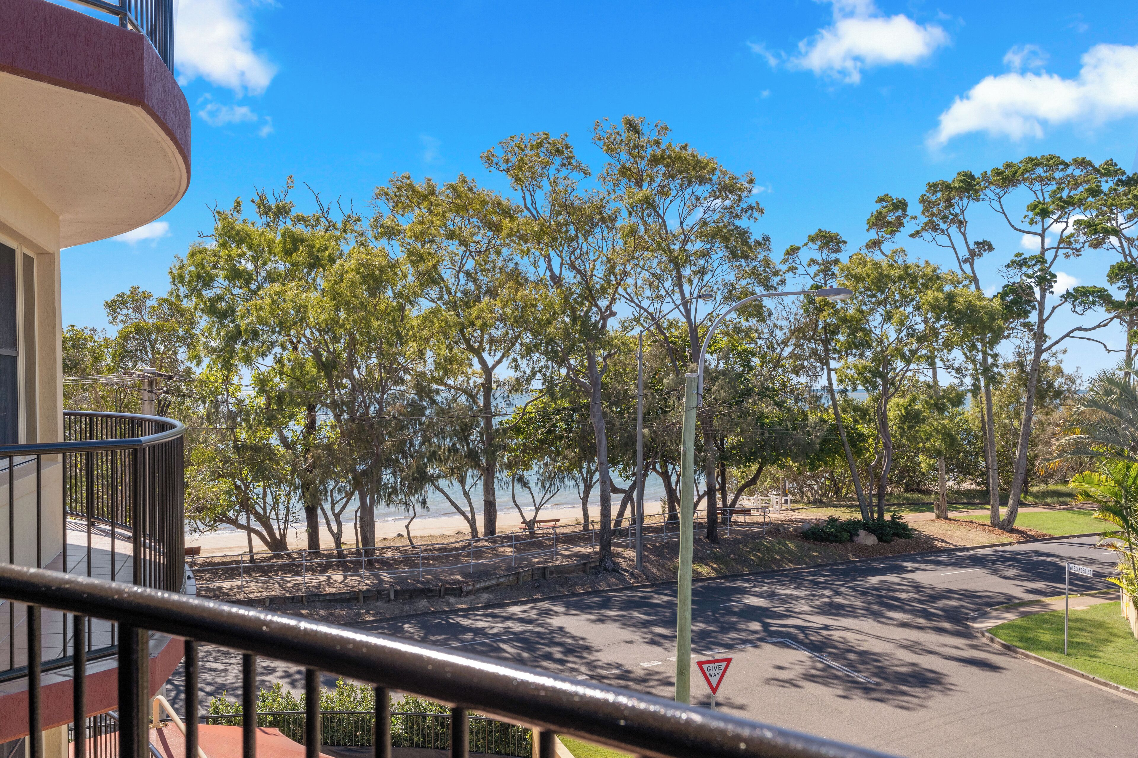 A balcony with a view of a beach, trees, and a road with a yield sign.