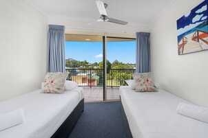 Habitación de hotel con dos camas, ventilador de techo y balcón con vista a la ciudad.