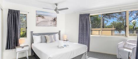 A modern hotel room with a large bed, a ceiling fan, a window with curtains, a bedside table with a lamp, and a view of the outdoors.