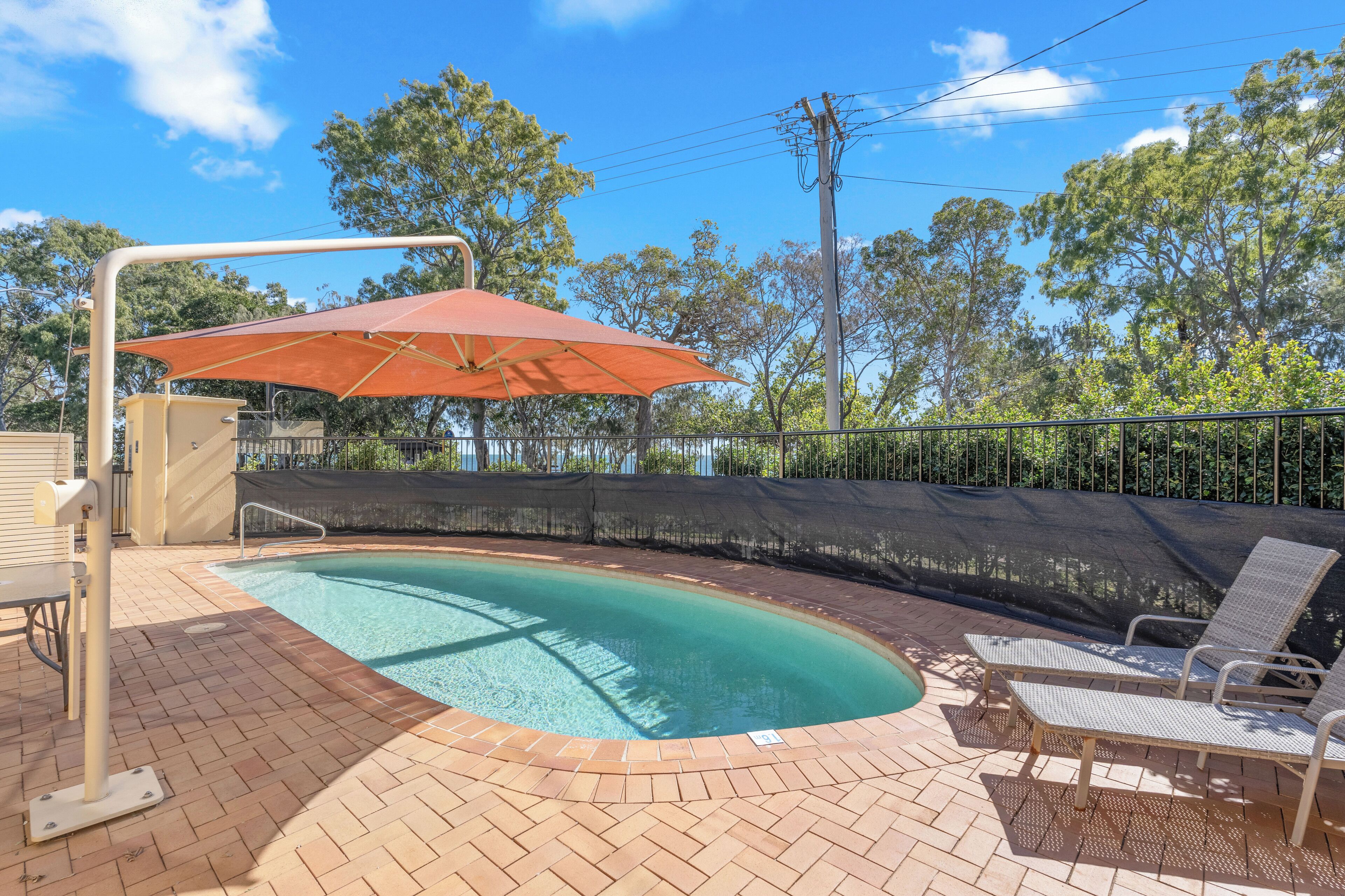 A swimming pool with a sunshade, lounge chairs, and a brick patio.
