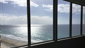 Vista del océano a través de amplias ventanas, con una playa en primer plano.